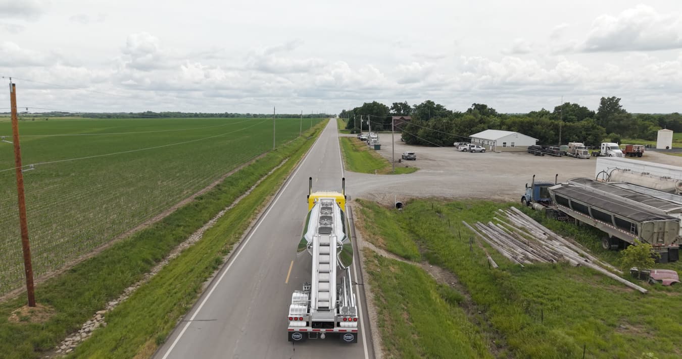 Aerial view of a pneumatic tank trailer on a two-lane highway approaching a plant.