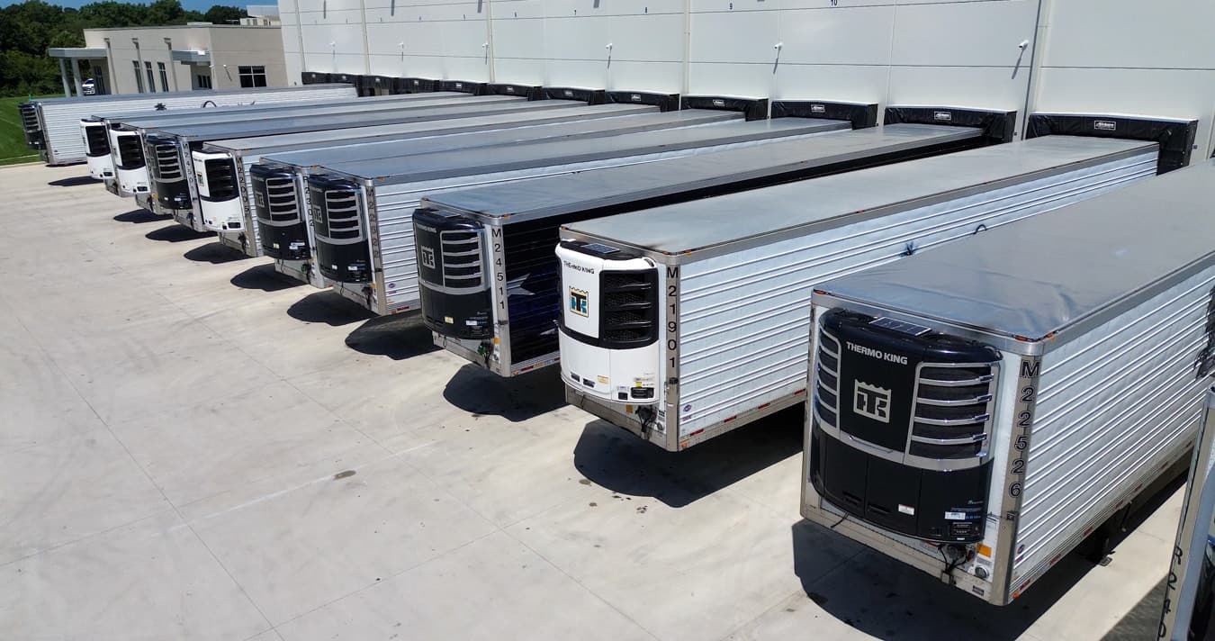 A row of refrigerated trailers backed into loading docks, reefer units facing the camera.