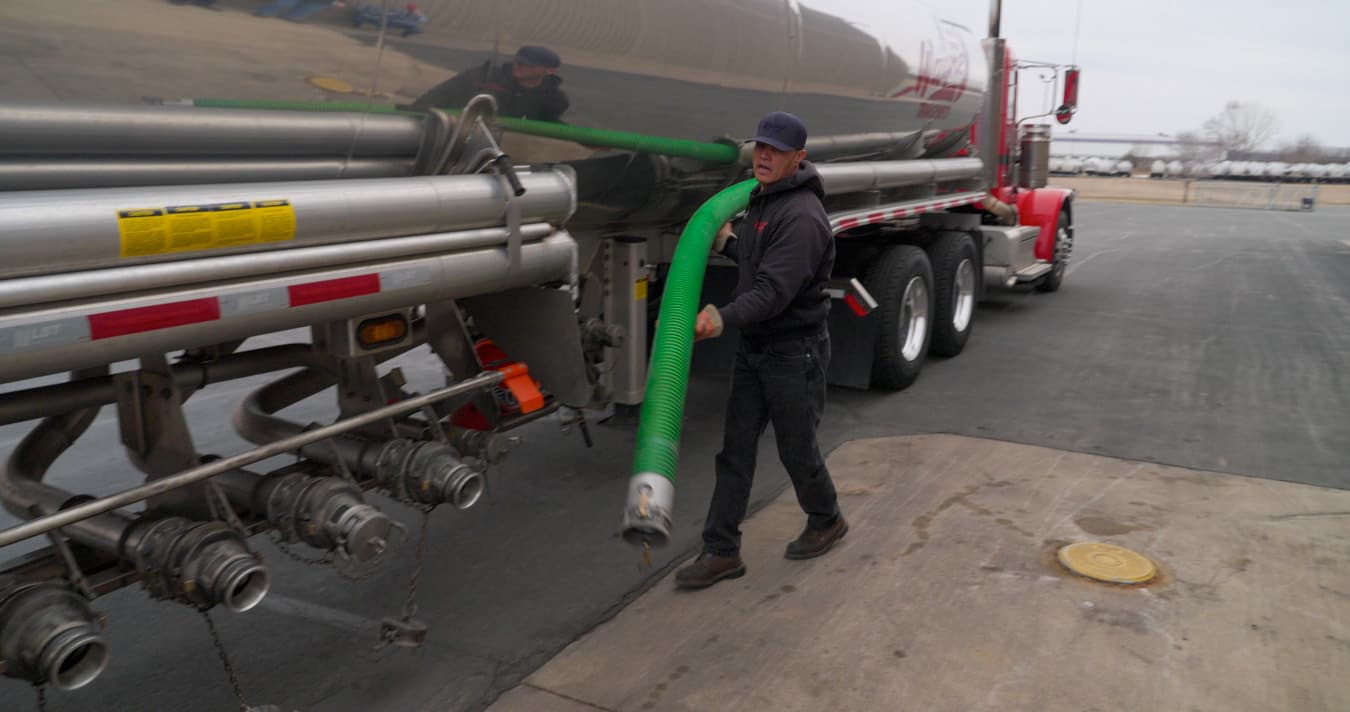 A driver connecting a discharge hose to a liquid tank trailer at a terminal.