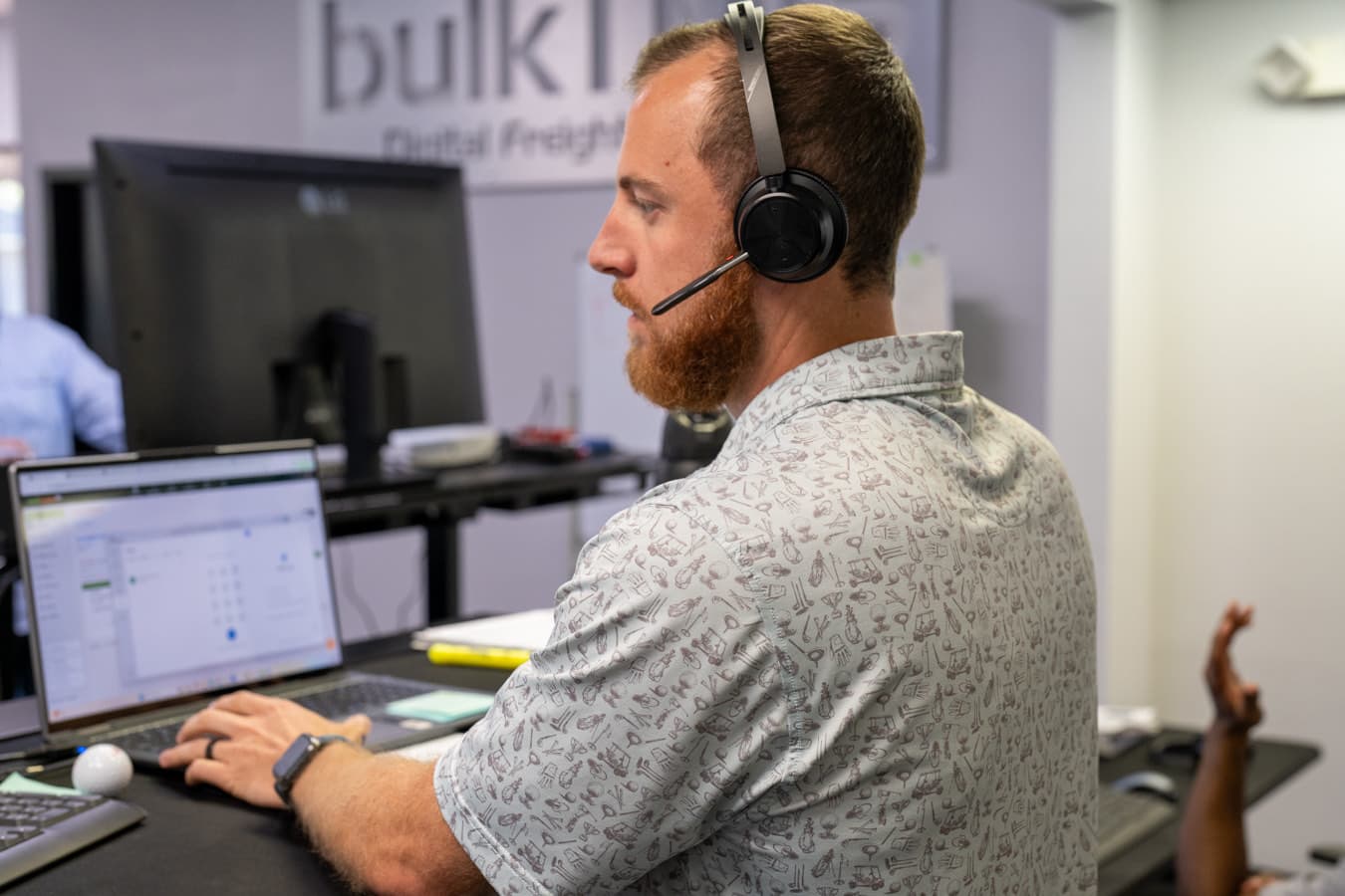 A member of the team working at a desk in the BulkLoads office, headset on, spreadsheet open.